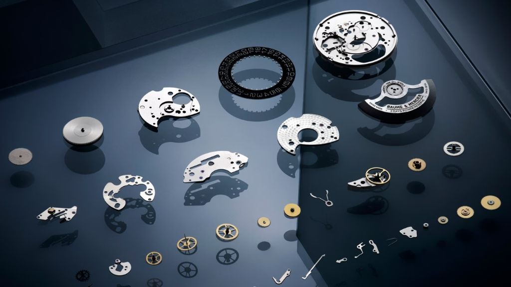 Alle onderdelen van Baume & Marcier horloge naast elkaar uitgestald op een blauwe doorzichtige plaat.