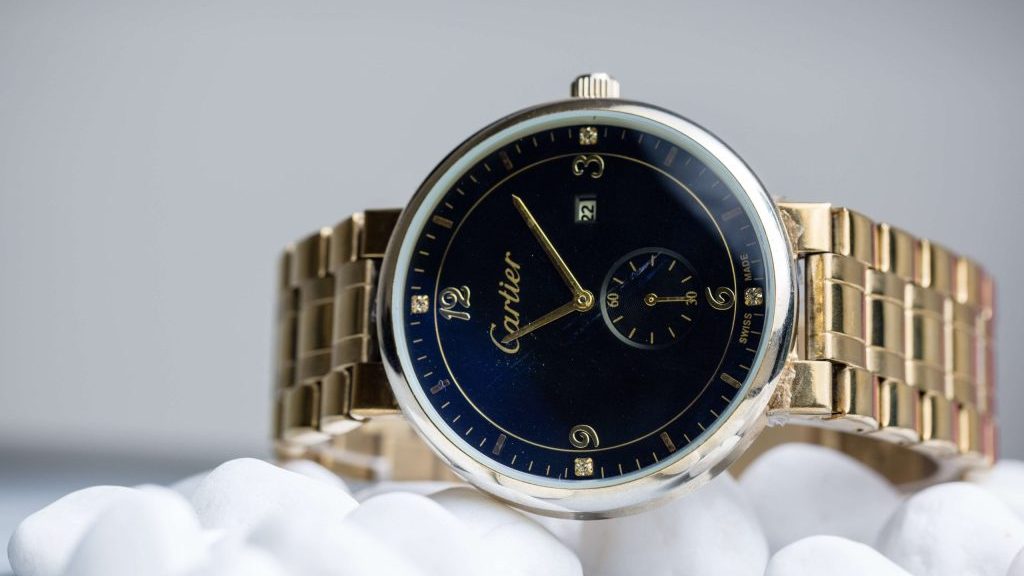 Cartier horloge met stalen kast, blauwe wijzerplaat en goudkleurige, stalen band op watten.