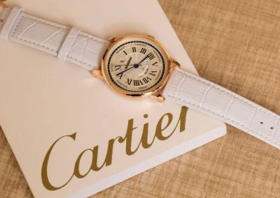 Modern Cartier horloge roségoud met witte band en wijzerplaat met zwarte details op wijzerplaat. Liggend op wit blokje met Cartier logo.