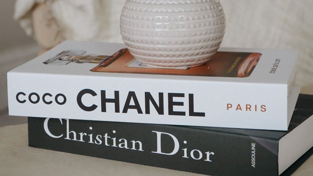 2 Chanel boeken schuin op elkaar met aas erop, 1 witte van Coco Chanel en 1 zwarte van Christian Dior