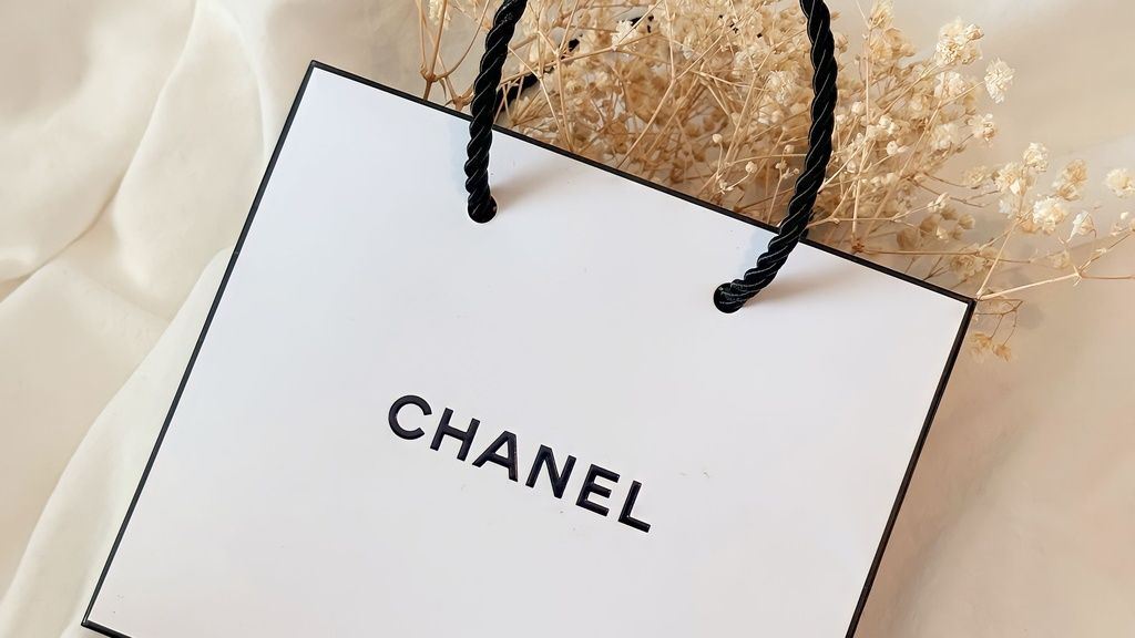 Chanel tas wit met zwart randje met gedroogde beige bloemen op wit bed