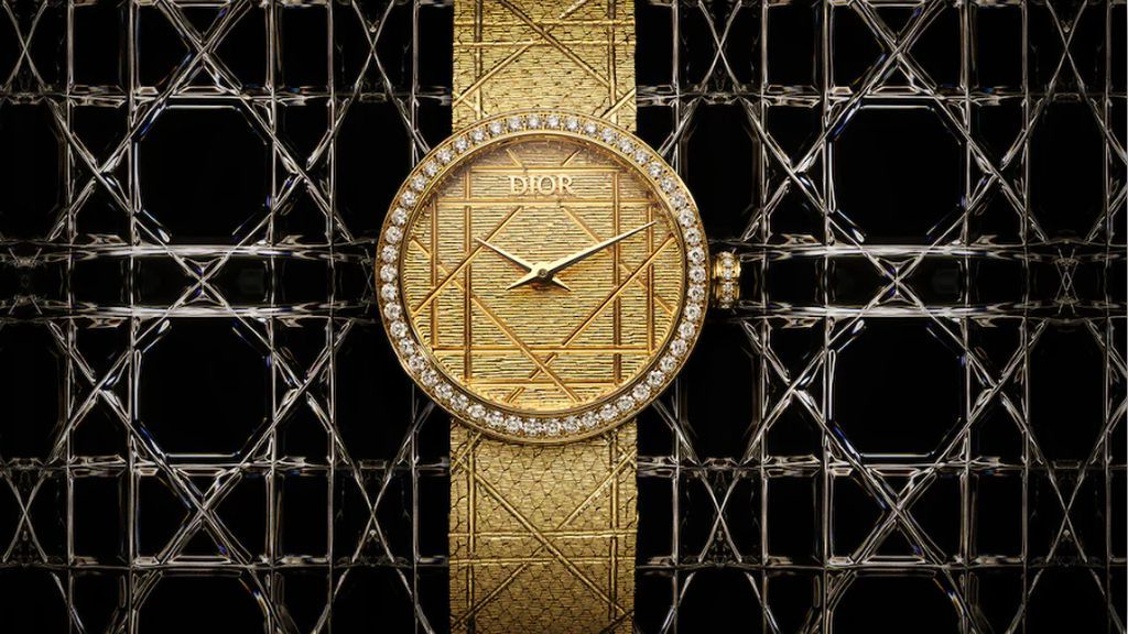 Geelgouden Christian Dior horloge met gouden wijzerplaat, gouden band met hand gegraveerde details en diamanten in lunetten staand plat op zwarte achtergrond met gouden motief erin.