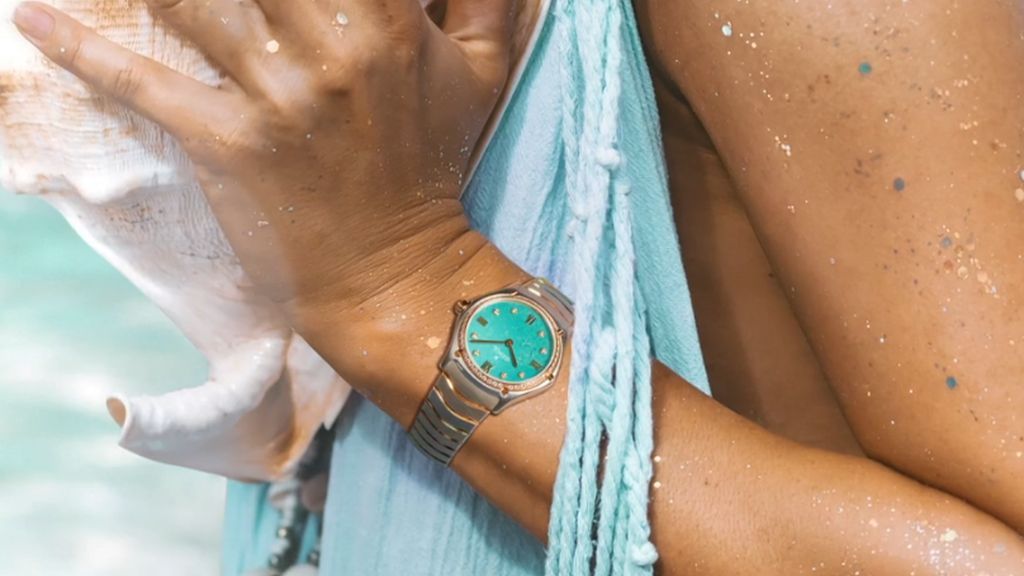 Stalen Ebel horloge met gouden lunette en digits en turqoise wijzerplaat om pols van vrouw die in het zwembad zit