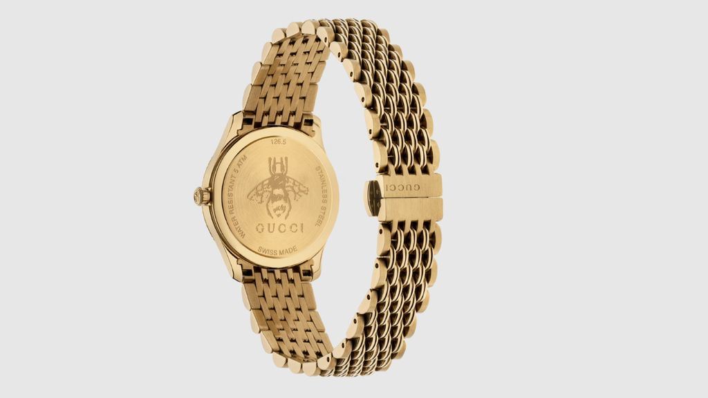 Gucci gold plated horloge, met goudkleurige horlogekast en band, en zilveren zongebrande wijzerplaat met gouden bij, achteraanzicht op licht grijze ondergrond.