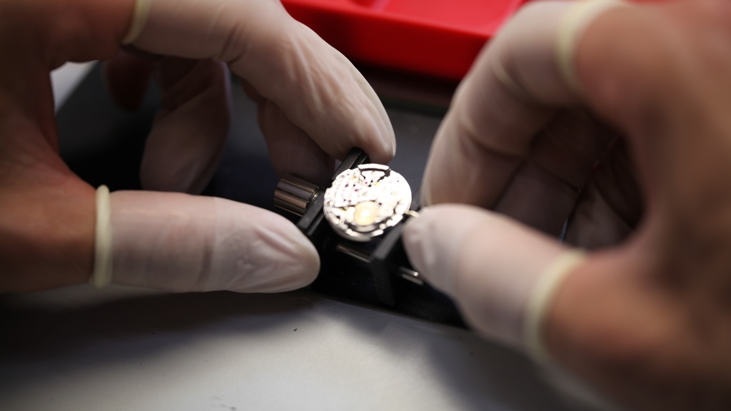 Uurwerk van Piaget horloge wordt afgesteld door horlogemaker met handschoenen aan met rode details op achtergrond.