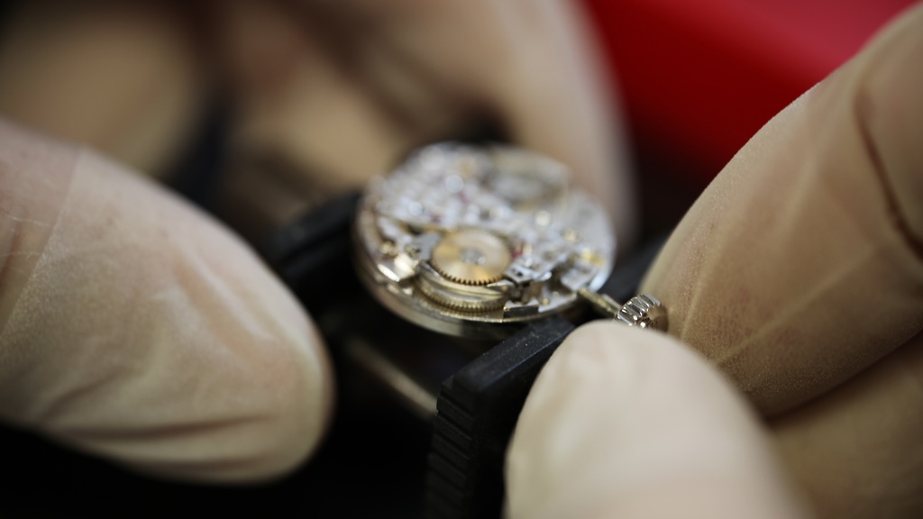 Uurwerkmaker stelt kroon en stift van Casio horloge met witte handschoenen aan met rode achtergrond.