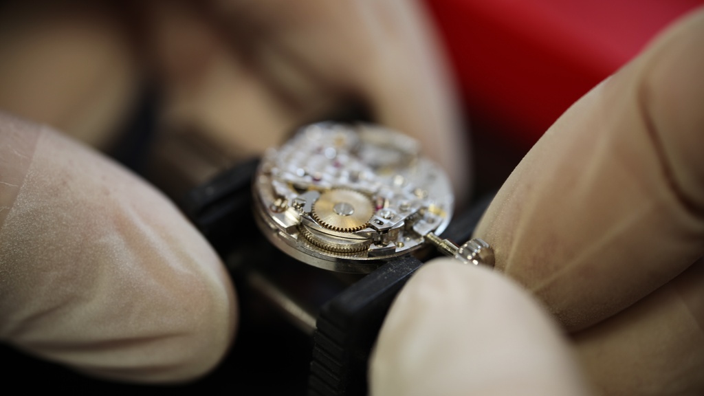 Uurwerkmaker stelt kroon en stift van Patek Philippe horloge met witte handschoenen aan met rode achtergrond.