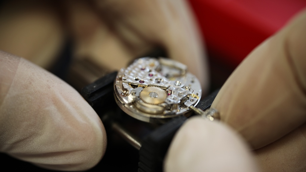 Horlogemaker repareert een Christian Dior uurwerk met witte handschoenen aan.