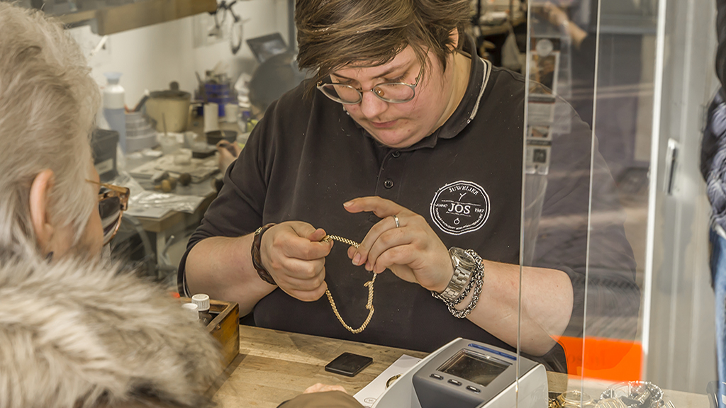 Rowan helpt klant aan balie en bekijkt gouden collier bij Edelsmederij Jos, het atelier en werkplaats van Juwelier Jos.
