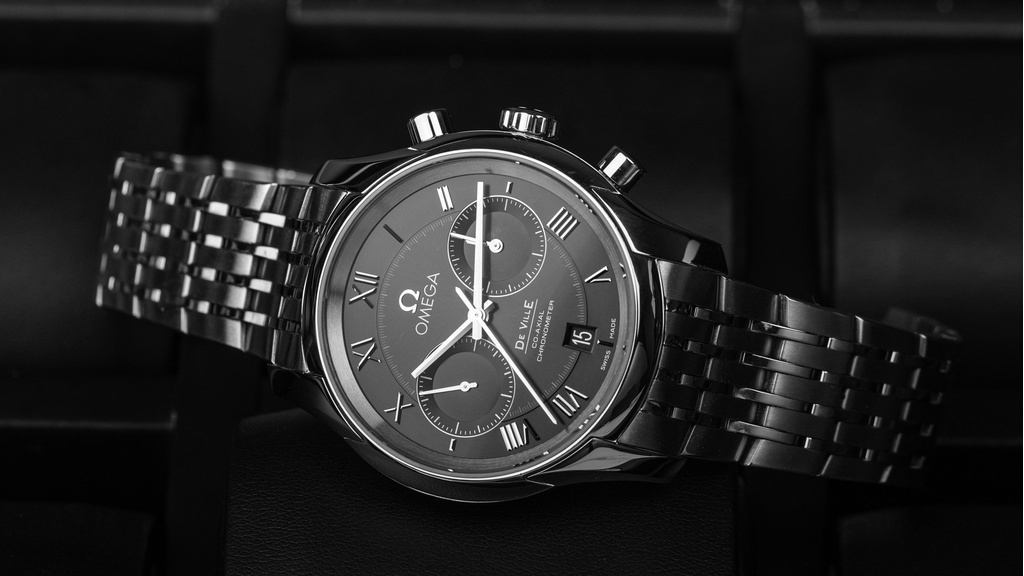 Omega horloge staal met donkergrijze wijzerplaat en witte wijzers op grijs leren achtergrond, zijaanzicht van horloge.