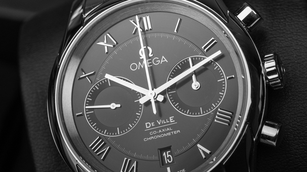 Omega horloge staal met donkergrijze wijzerplaat en witte wijzers op grijs leren achtergrond, close up van deel wijzerplaat.