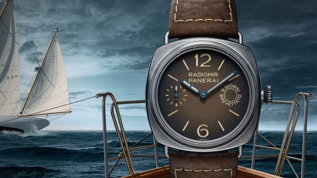 Panerai horloge met grijze kast en kroon en donkerbruine band en wijzerplaat met zee en boten en deel van schip als achtergrond.