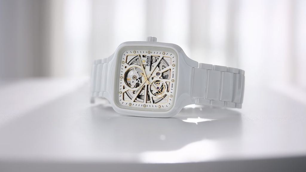Wit keramieken Rado horloge met zichtbaar uurwerk als wijzerplaat, liggend op witte steen.