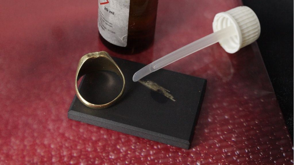 Toetssteen met gouden ring, streep en flesje met chemicalien om karaat goud te bepalen