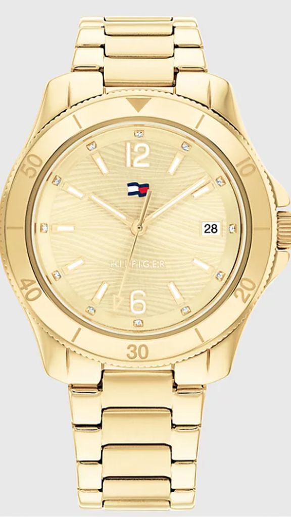 Vooraanzicht van goudkleurig Tommy Hilfiger horloge met goudkleurige wijzerplaat, lunette en band en witte details op wijzerplaat en logo van Tommy Hilliger, horloge op lichtgrijze achtergrond.