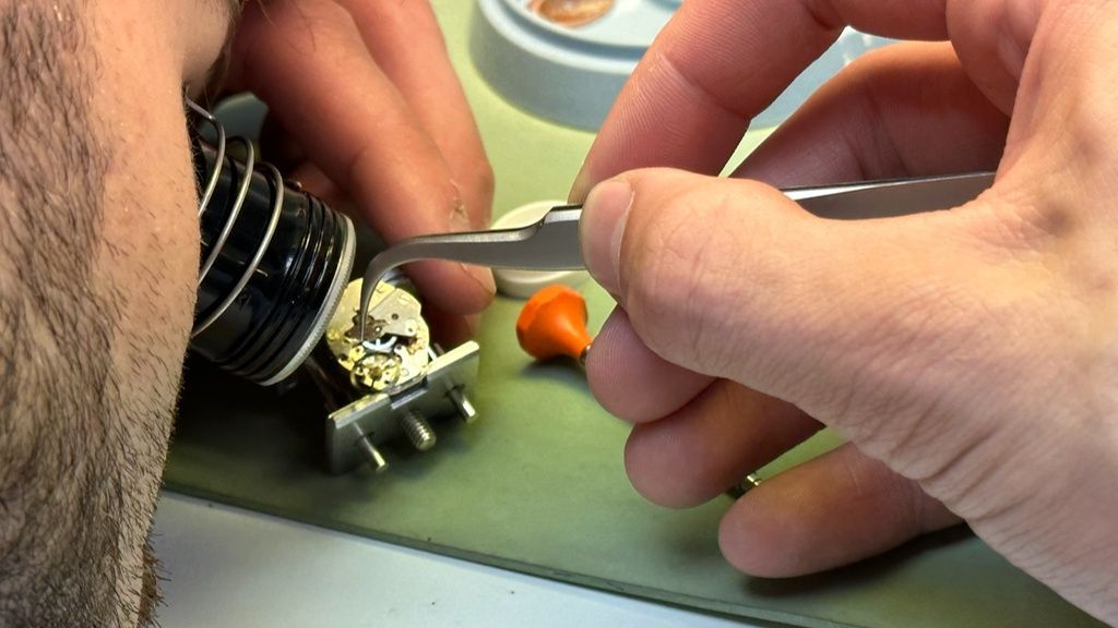 Uurwerkmaker repareert Breitling uurwerk met pincet en loep