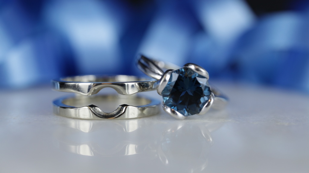 Witgouden combi ring met topaas in solitair zetting. Ringen kunnen uit elkaar gedragen worden, zowel los als in elkaar op glanzende grijze ondergrond en blauwe lint achtergrond