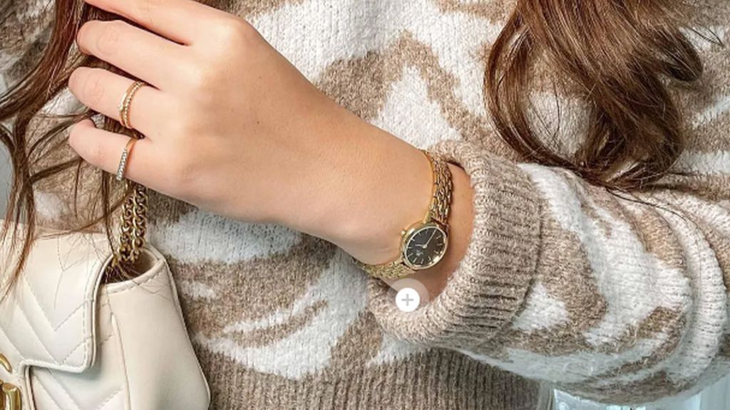 Danish Design horloge met geelgouden kast en band, zwarte wijzerplaat om pols van vrouw met zebra trui aan in lichtbeige en wit, beige tas met gouden accenten en gekruld bruin haar.