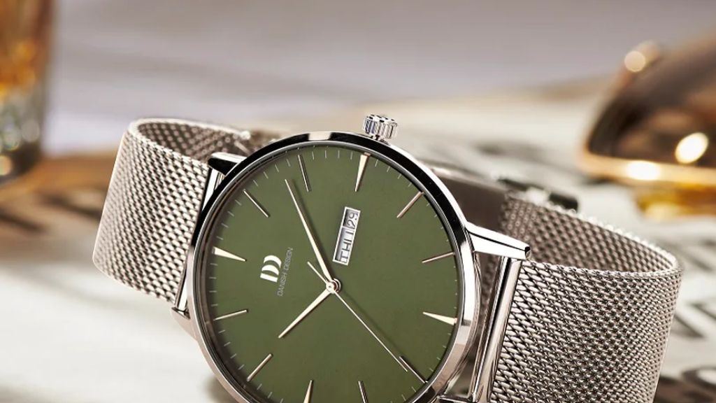Stalen Dnish Design horloge met milanese stalen band en groene wijzerplaat liggend op werkband met gereedschap op achtergrond.