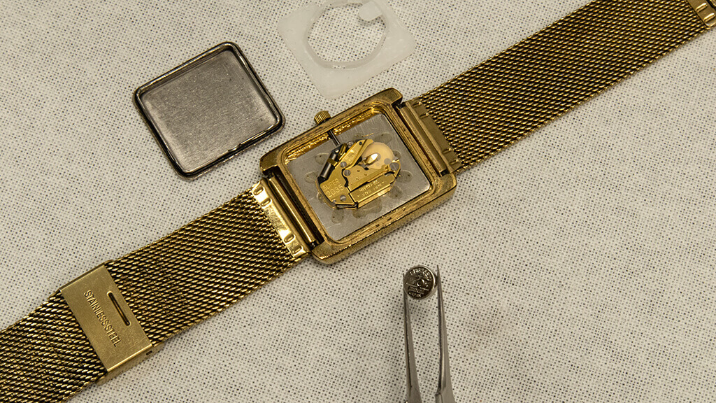 Goudkleurig horloge met open achterkant wordt nieuwe horloge batterij ingeplaatst.