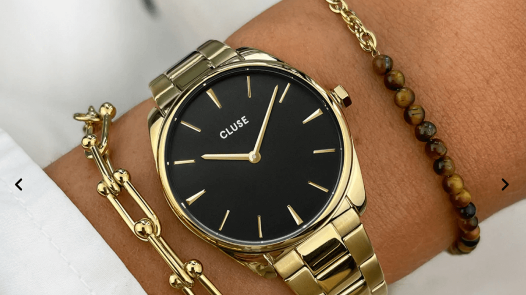 Geelgouden Cluse horloge met zwarte wijzerplaat om pols met geelgouden schakelarmband ernaast Geelgouden Cluse horloge met zwarte wijzerplaat om pols met geelgouden schakelarmband ernaast